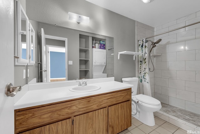 bathroom with tile patterned floors, walk in shower, vanity, toilet, and stacked washer / drying machine