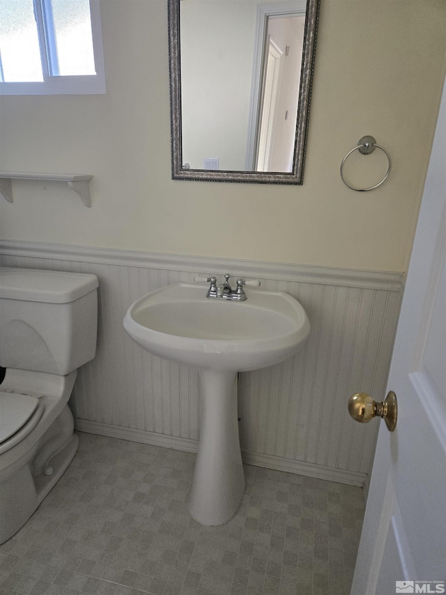 half bath with a wainscoted wall, a sink, and toilet