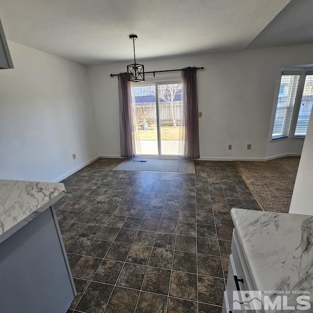 unfurnished dining area with baseboards, an inviting chandelier, and a healthy amount of sunlight