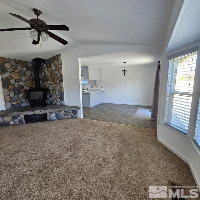 unfurnished living room with carpet floors, a wood stove, vaulted ceiling, and ceiling fan