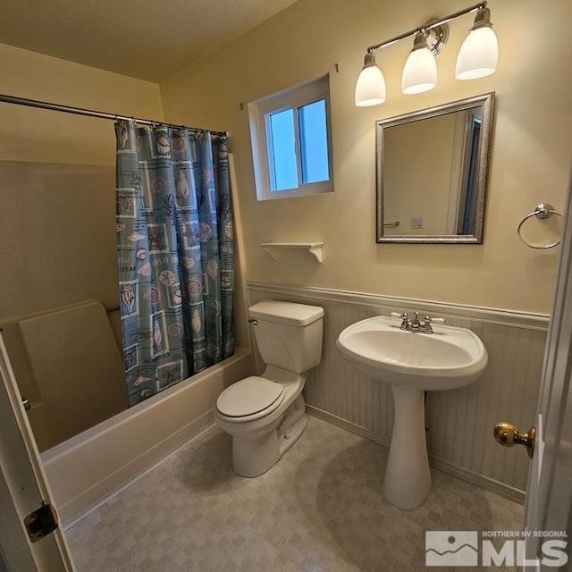 full bath featuring a wainscoted wall, a sink, shower / bathtub combination with curtain, and toilet