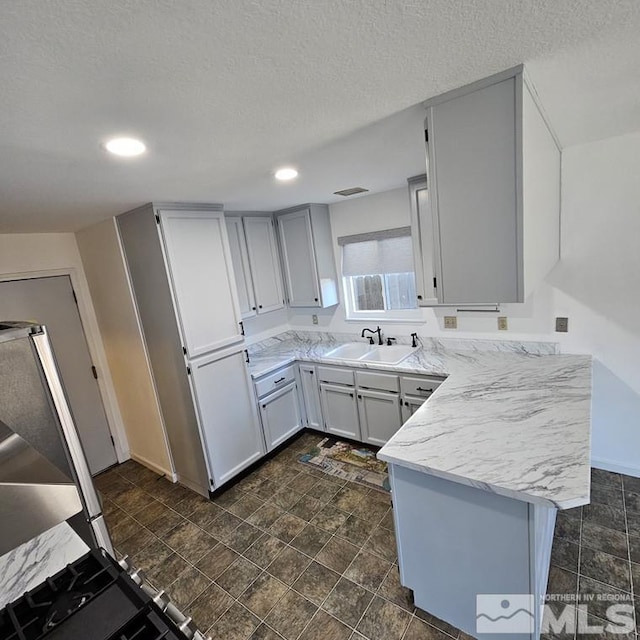 kitchen featuring recessed lighting, visible vents, a sink, a textured ceiling, and a peninsula