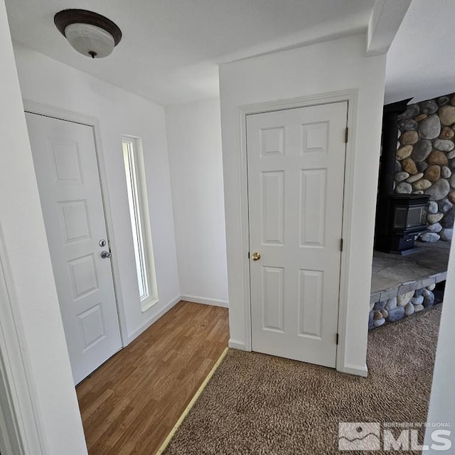 carpeted entryway with a wood stove, baseboards, and wood finished floors