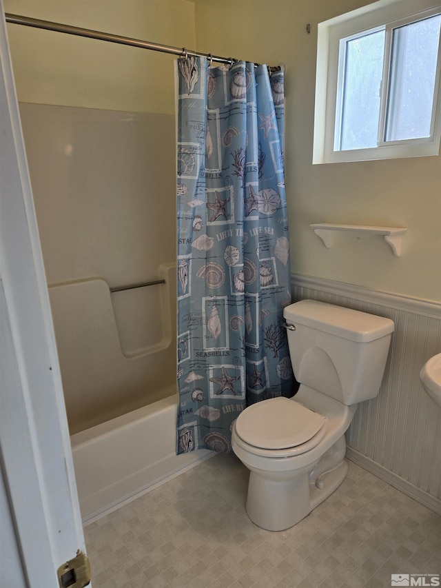 full bathroom featuring wainscoting, shower / bath combo with shower curtain, toilet, and tile patterned floors