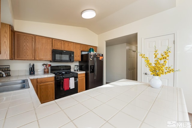 kitchen featuring tile counters, black appliances, vaulted ceiling, and sink