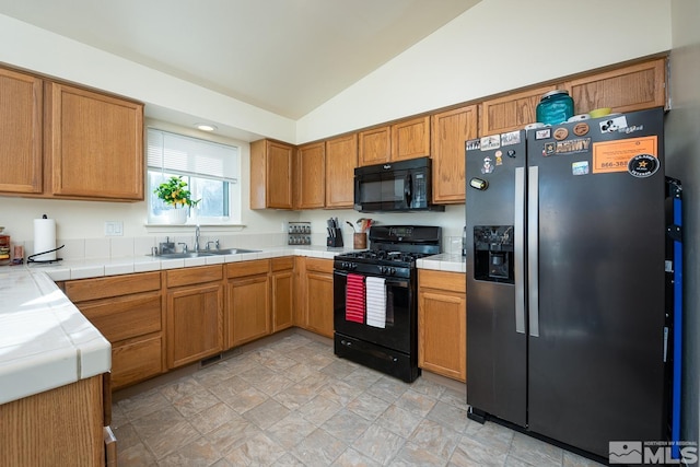 kitchen featuring sink, tile countertops, lofted ceiling, and black appliances