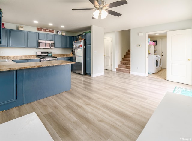 kitchen with washer and dryer, light hardwood / wood-style floors, blue cabinetry, and appliances with stainless steel finishes