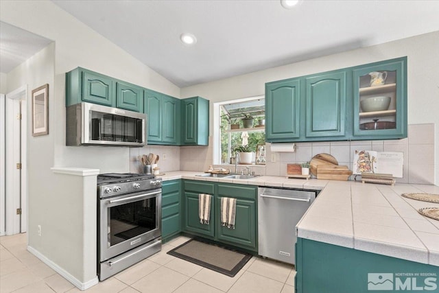 kitchen featuring tile countertops, lofted ceiling, decorative backsplash, light tile patterned floors, and stainless steel appliances