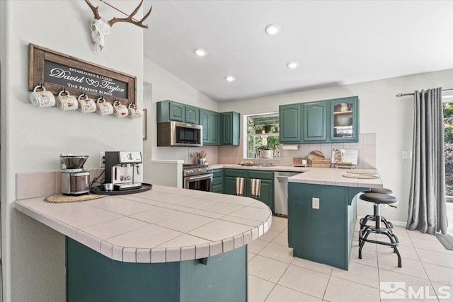 kitchen with tile countertops, kitchen peninsula, vaulted ceiling, a breakfast bar, and appliances with stainless steel finishes