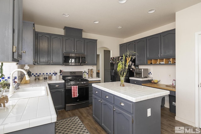 kitchen featuring sink, a center island, dark wood-type flooring, tile countertops, and appliances with stainless steel finishes