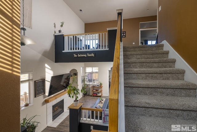 stairway with a tiled fireplace, a towering ceiling, and hardwood / wood-style flooring