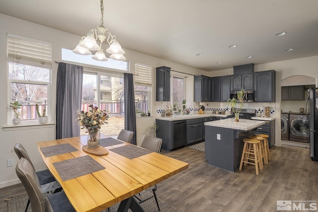 kitchen with washing machine and dryer, dark hardwood / wood-style flooring, pendant lighting, a kitchen island, and appliances with stainless steel finishes