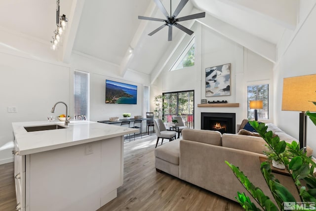 living room with high vaulted ceiling, sink, ceiling fan, light wood-type flooring, and beam ceiling