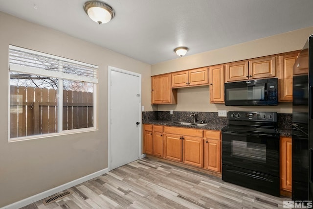 kitchen with sink, light hardwood / wood-style floors, dark stone countertops, and black appliances