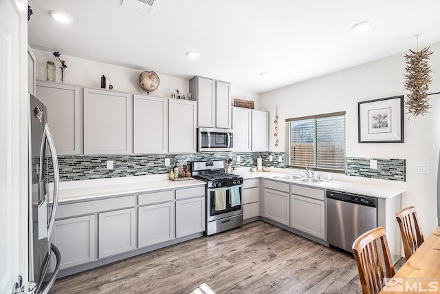 kitchen featuring appliances with stainless steel finishes, backsplash, sink, light hardwood / wood-style flooring, and gray cabinets