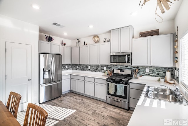 kitchen featuring appliances with stainless steel finishes, tasteful backsplash, light hardwood / wood-style flooring, and sink