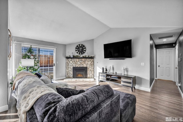 living room featuring a stone fireplace, hardwood / wood-style floors, and lofted ceiling