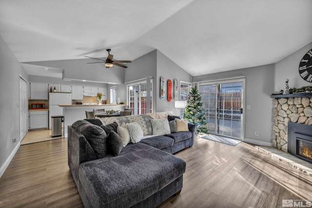 living room featuring ceiling fan, light hardwood / wood-style floors, a stone fireplace, and vaulted ceiling