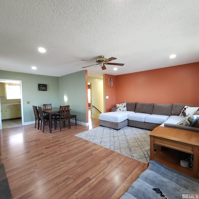 living room featuring a textured ceiling, light wood-type flooring, and ceiling fan