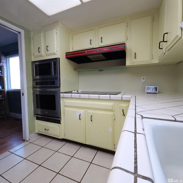 kitchen featuring tile counters, light tile patterned floors, appliances with stainless steel finishes, and cream cabinets