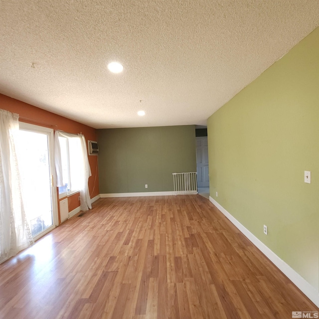 unfurnished room with a wall mounted air conditioner, a textured ceiling, and light hardwood / wood-style flooring