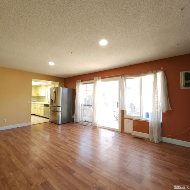 unfurnished living room with a textured ceiling, light hardwood / wood-style flooring, and an AC wall unit