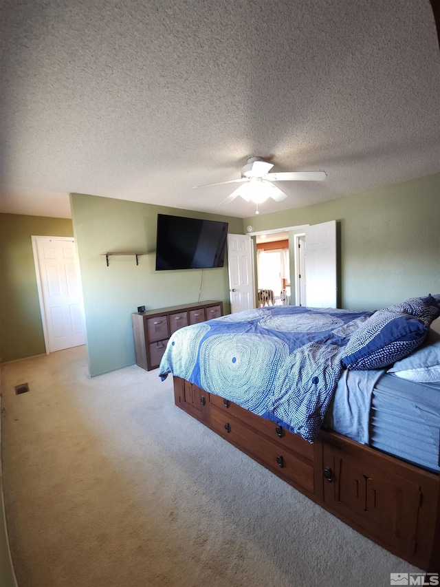 bedroom with ceiling fan, light colored carpet, and a textured ceiling