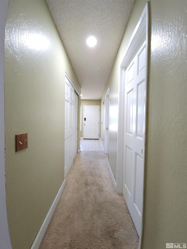 corridor featuring light colored carpet and a textured ceiling