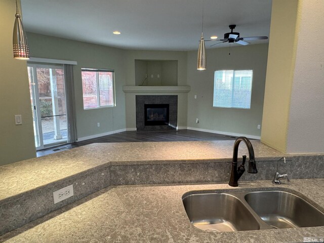 kitchen featuring ceiling fan, sink, a fireplace, hardwood / wood-style floors, and hanging light fixtures