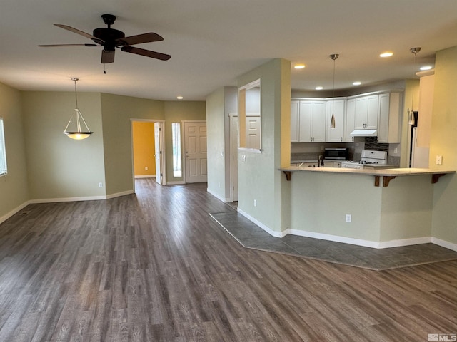 kitchen with kitchen peninsula, stove, dark hardwood / wood-style flooring, a kitchen breakfast bar, and white cabinets