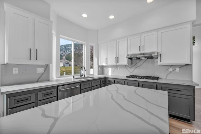 kitchen with dishwasher, sink, light hardwood / wood-style flooring, light stone counters, and gas cooktop