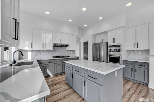 kitchen featuring appliances with stainless steel finishes, light stone counters, sink, light hardwood / wood-style flooring, and a center island