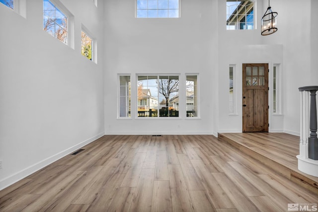 foyer featuring a high ceiling, light wood-type flooring, a wealth of natural light, and a notable chandelier