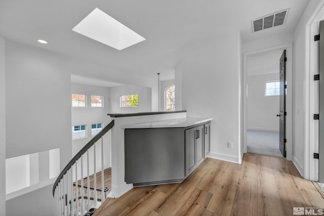 corridor with a skylight, plenty of natural light, and light wood-type flooring