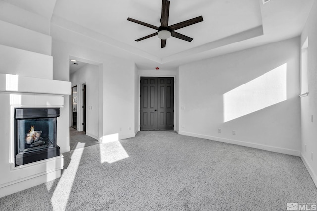 unfurnished living room with ceiling fan, a raised ceiling, and light carpet