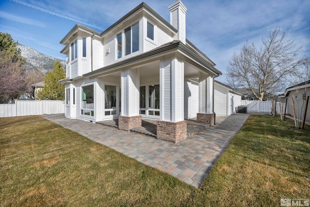 rear view of house with central AC unit, a mountain view, a patio area, and a yard