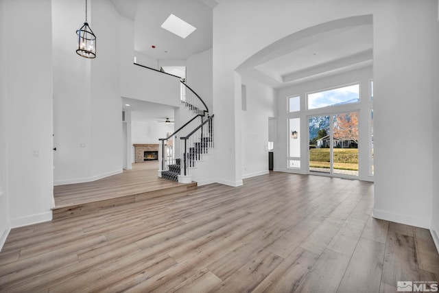 foyer entrance featuring ceiling fan with notable chandelier, a towering ceiling, and light wood-type flooring