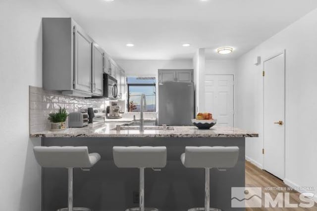 kitchen with stainless steel refrigerator, gray cabinets, kitchen peninsula, and hardwood / wood-style flooring