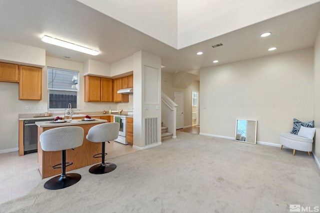 kitchen featuring light carpet, a kitchen bar, electric stove, dishwasher, and a center island