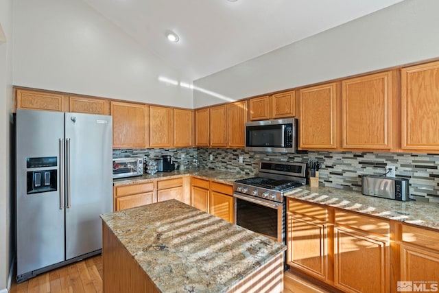 kitchen featuring a kitchen island, appliances with stainless steel finishes, tasteful backsplash, light hardwood / wood-style floors, and light stone counters