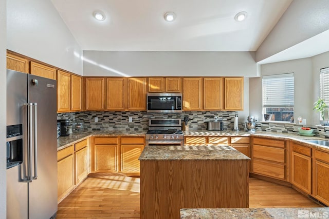 kitchen featuring light wood-type flooring, backsplash, stainless steel appliances, a kitchen island, and lofted ceiling