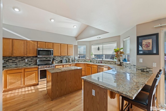 kitchen featuring kitchen peninsula, a kitchen breakfast bar, decorative backsplash, stainless steel appliances, and vaulted ceiling