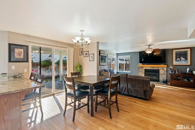 dining space featuring a stone fireplace, light hardwood / wood-style floors, and ceiling fan with notable chandelier