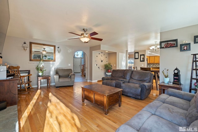 living room featuring ceiling fan with notable chandelier, light wood-type flooring, and plenty of natural light