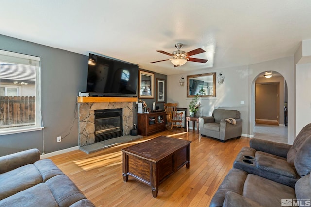 living room featuring ceiling fan, a stone fireplace, and light hardwood / wood-style flooring