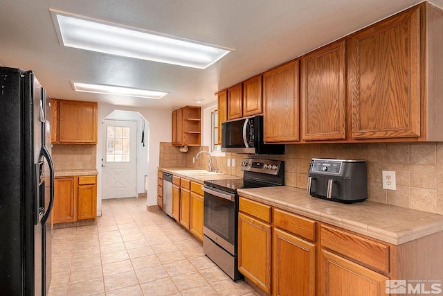 kitchen with decorative backsplash, stainless steel appliances, sink, light tile patterned floors, and tile counters