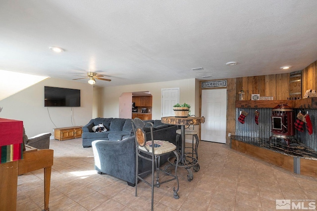 living room with ceiling fan, a textured ceiling, and wooden walls