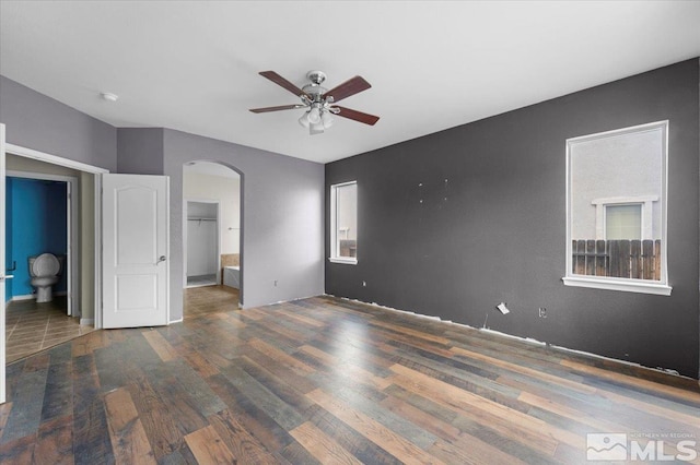 unfurnished bedroom featuring arched walkways, a ceiling fan, wood finished floors, and connected bathroom