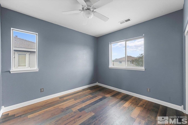spare room featuring visible vents, a ceiling fan, dark wood-style flooring, and baseboards