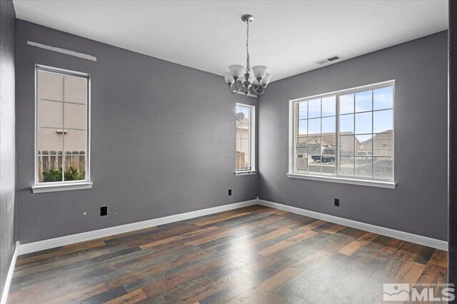 unfurnished room with baseboards, a notable chandelier, visible vents, and wood finished floors